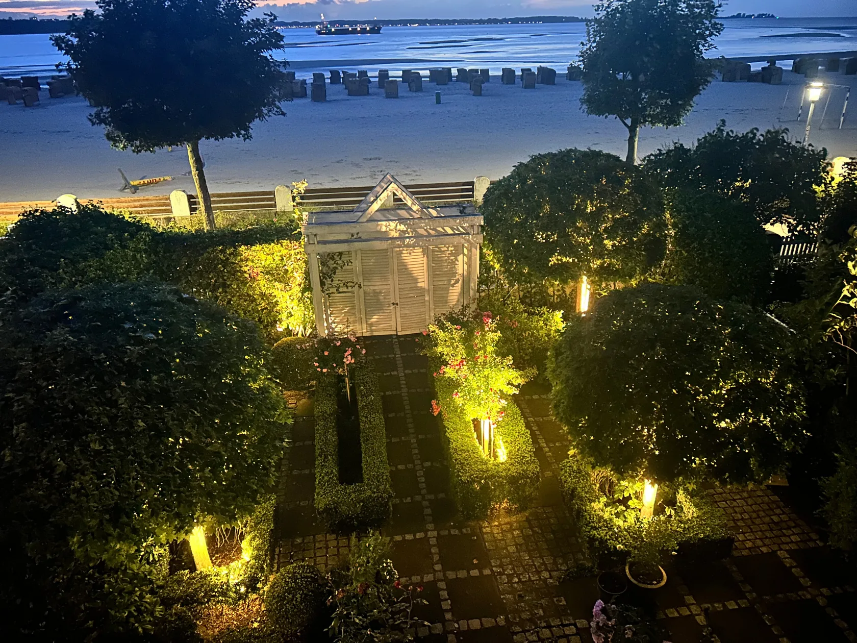 Gartenbeleuchtung für Kiel 1 Abendbeleuchtung in einem bepflanzten Privatgarten mit Gehölzen, Wegen und Blick auf das Wasser